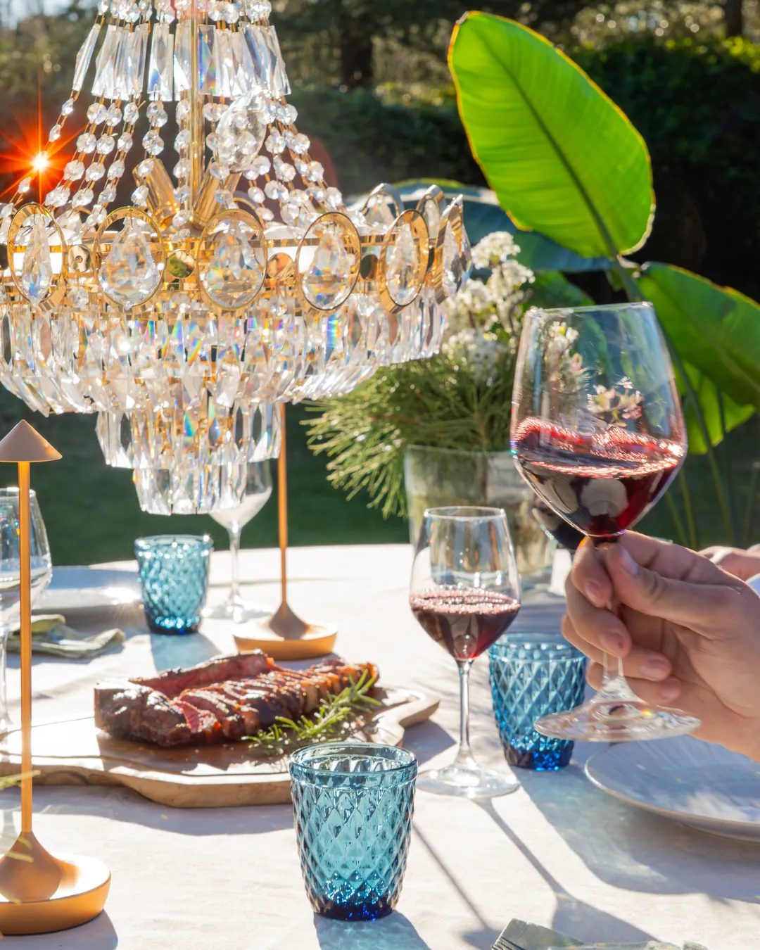 Primer plano de perfil de una invitada bebiendo vino tinto con un fondo de vegetación y palmeras difuminadas por la luz del sol