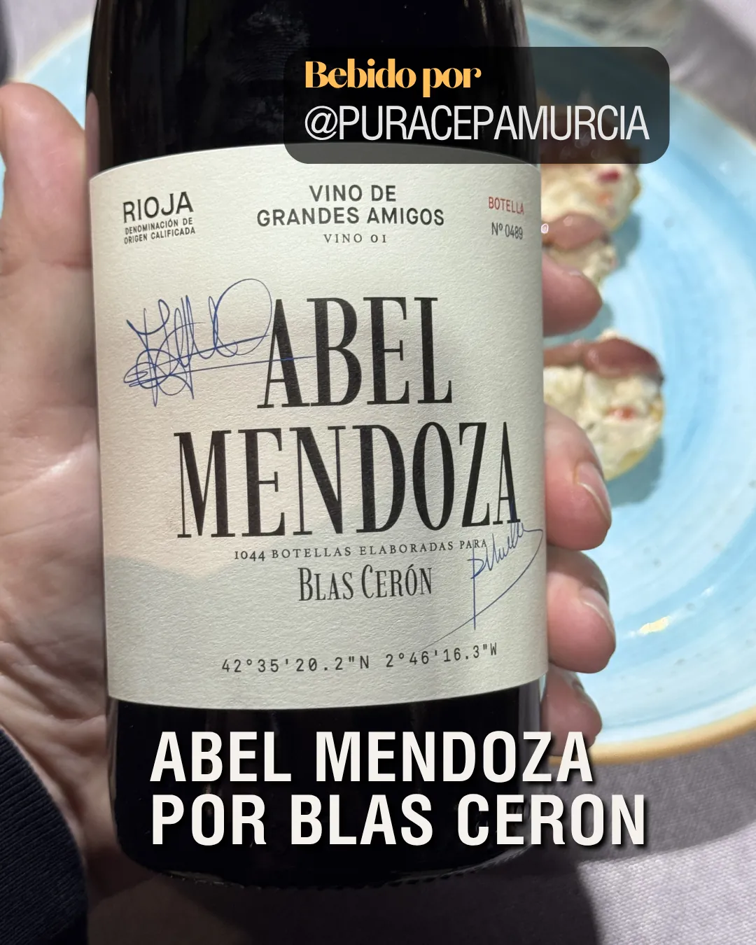 Mano sosteniendo una botella de vino Abel Mendoza por Blas Cerón con etiqueta blanca firmada, recomendado por Puracepamurcia