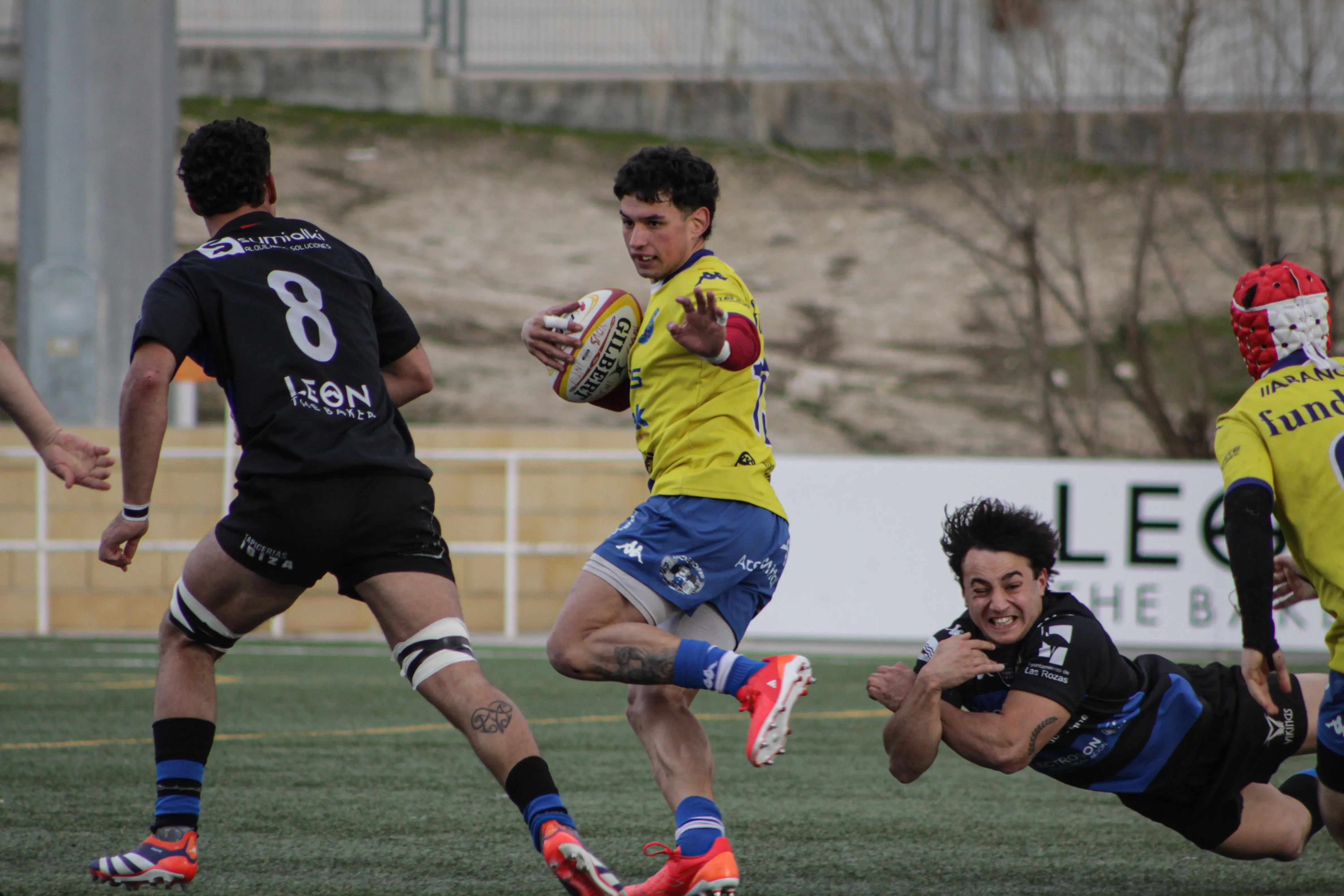 Acción de ataque con un jugador esquivando un placaje en un partido de rugby.