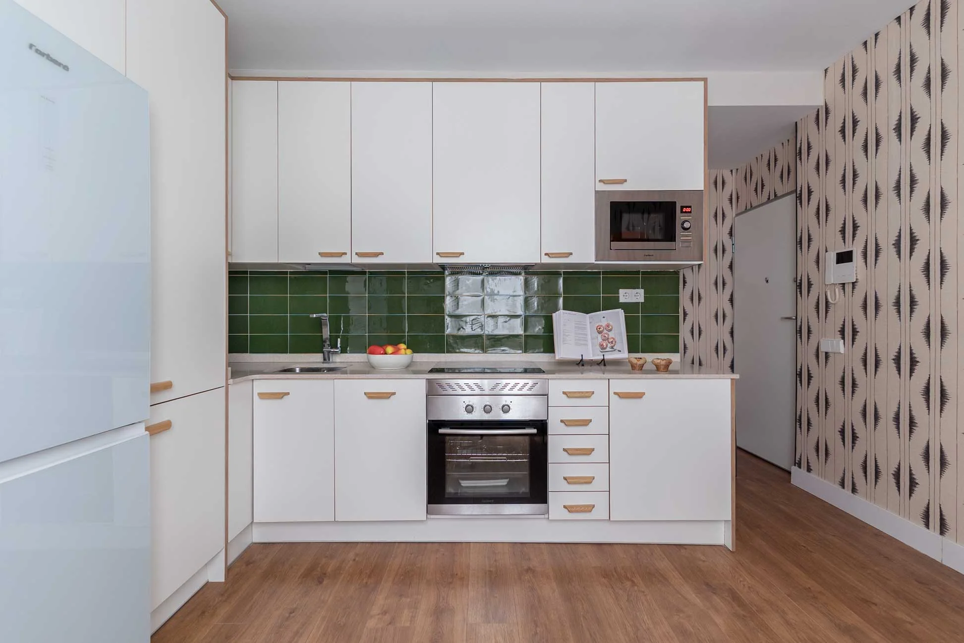 Plano frontal y simétrico de la cocina con muebles blancos, encimera clara, azulejo verde, horno, microondas integrado y frigorífico.
