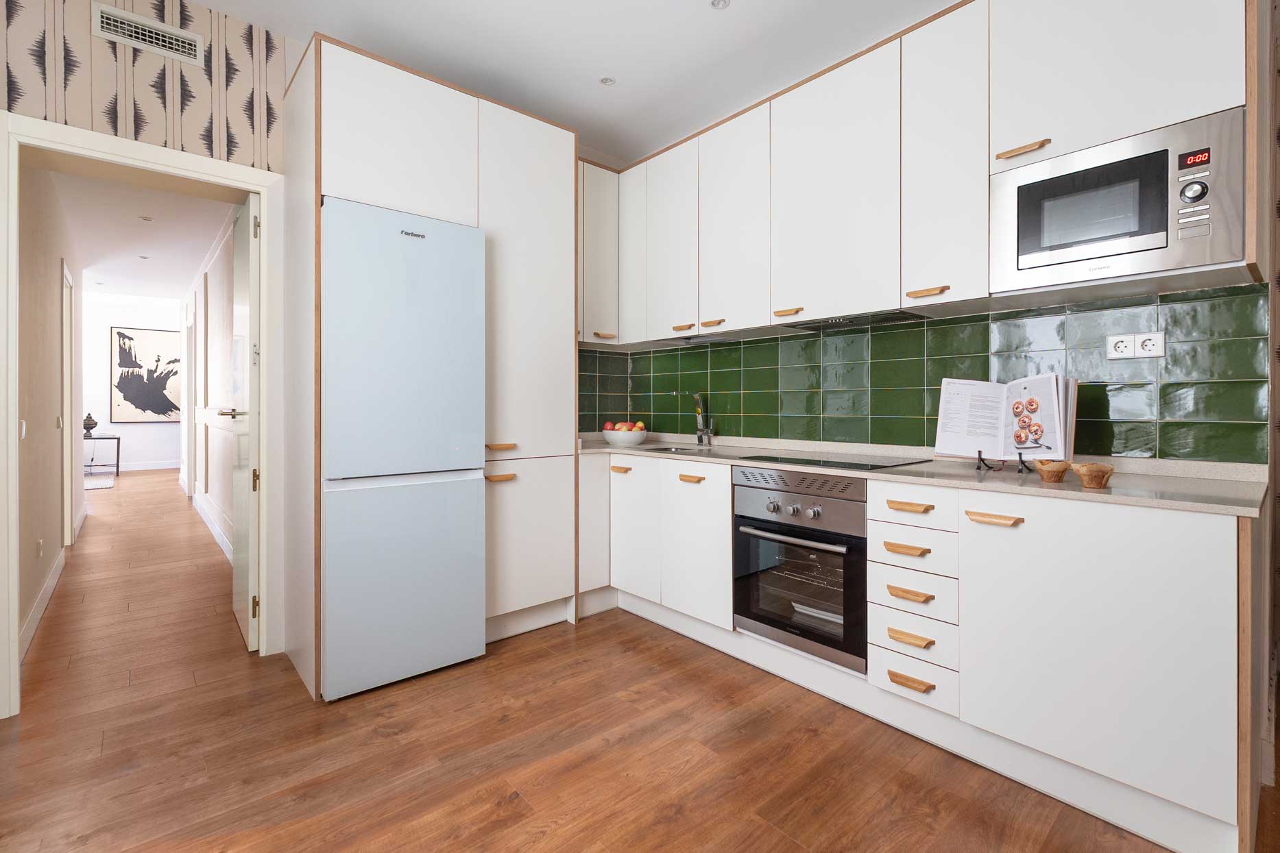 Perspectiva angular de la cocina con el frigorífico integrado y apertura visual hacia el pasillo distribuidor de la vivienda.