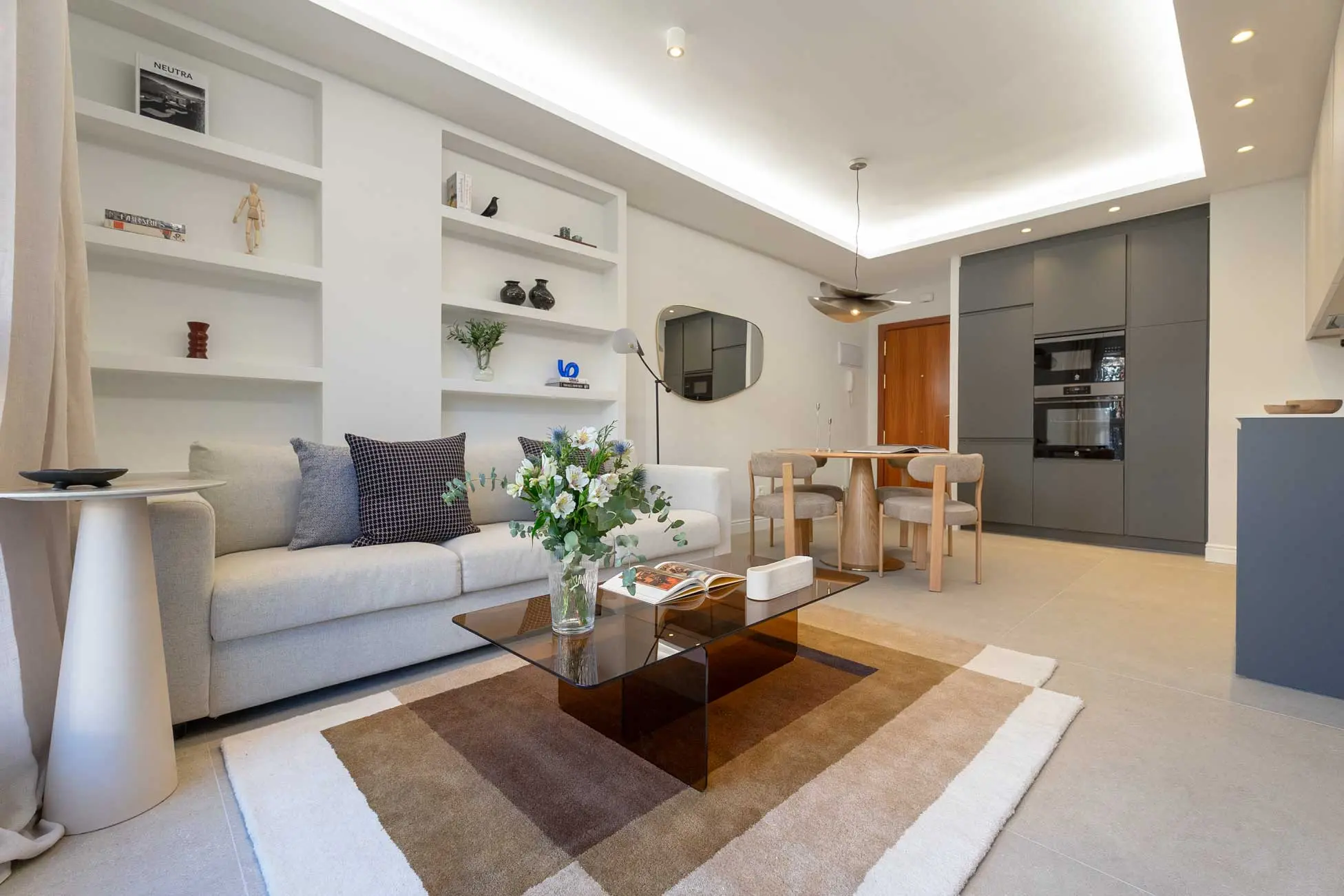 Plano general abierto del salón de diseño contemporáneo integrado con la zona de comedor, destacando una mesa de centro de cristal ahumado y mobiliario en tonos neutros.