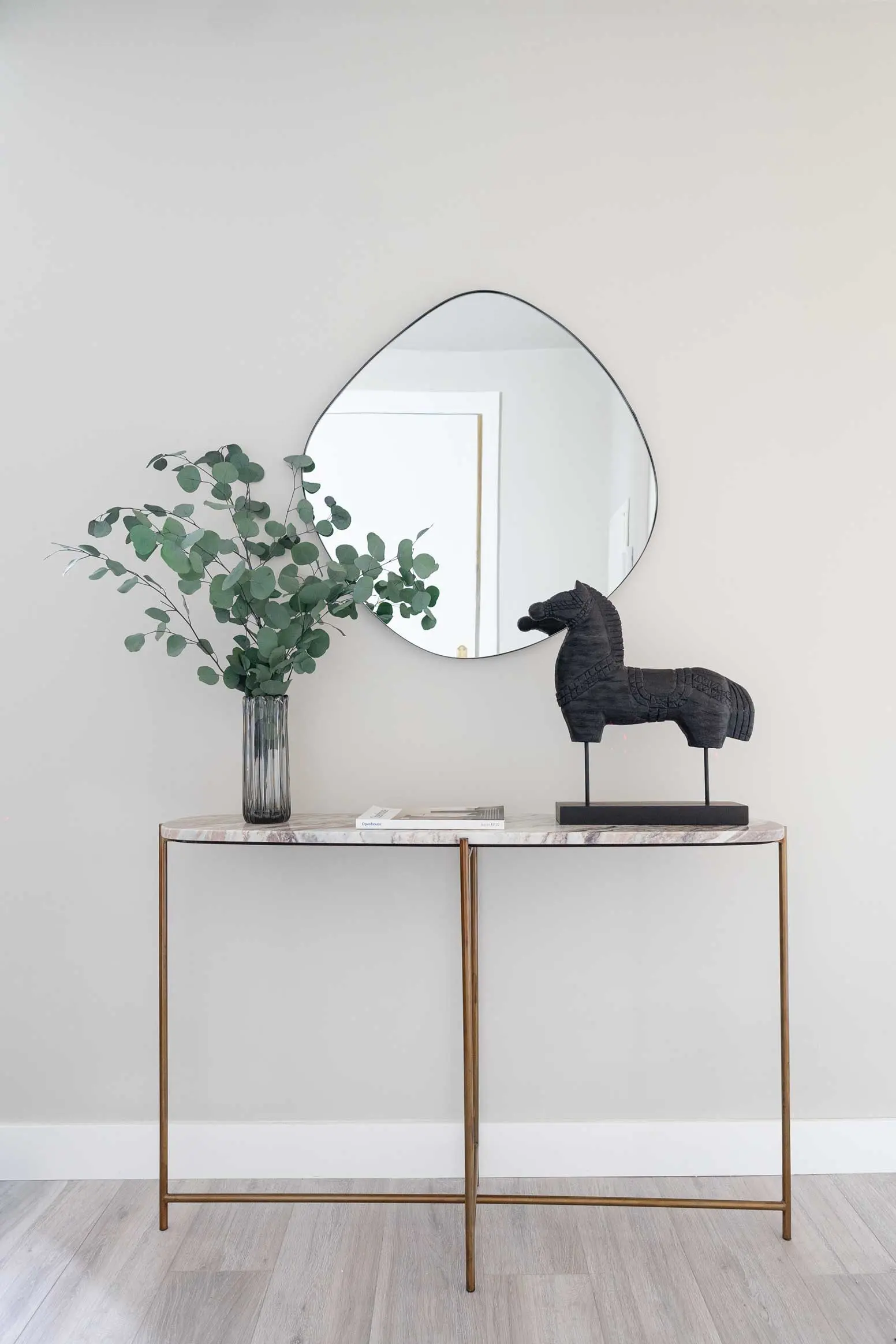 Detalle del mueble recibidor de la entrada con espejo curvo, jarrón con eucalipto y figura decorativa