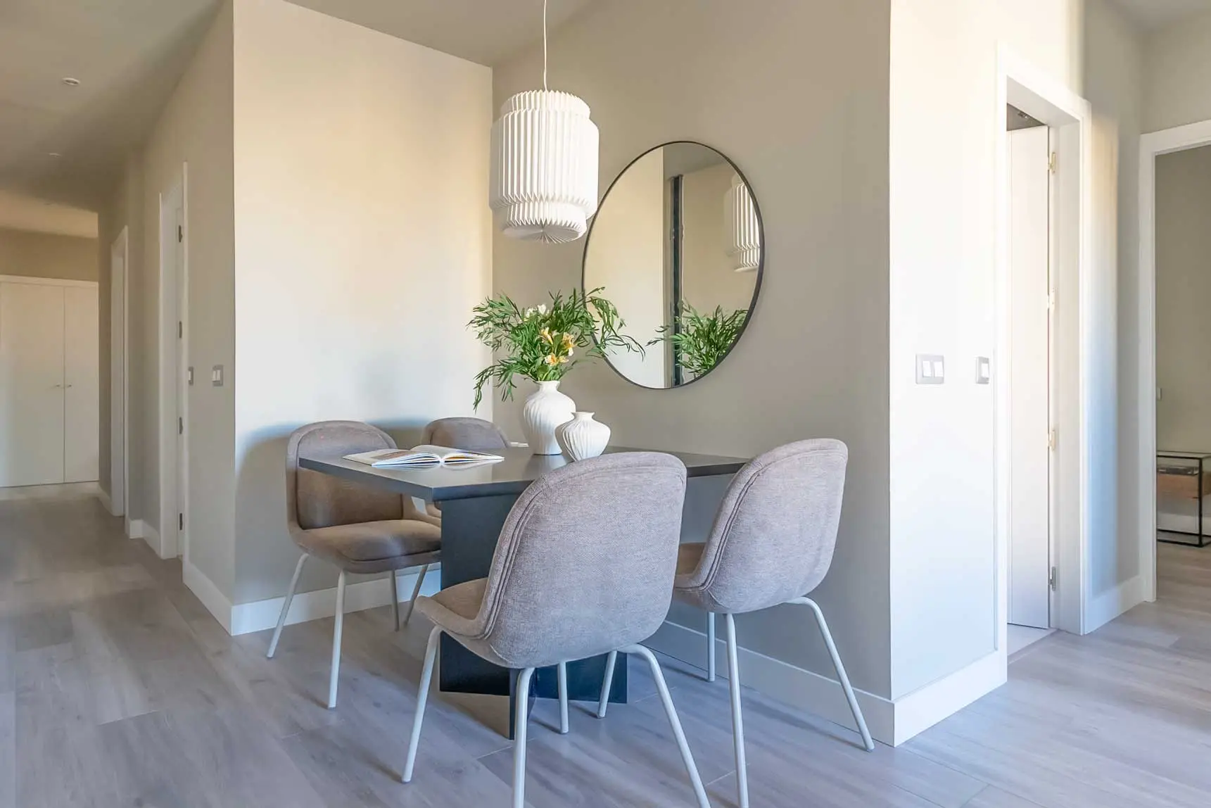 Zona del comedor con mesa moderna para cuatro comensales, lámpara de diseño plisada y espejo redondo