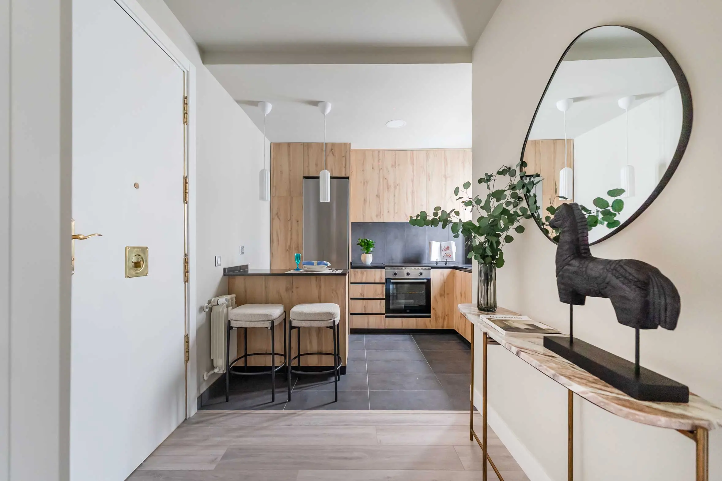 Perspectiva desde la entrada hacia la cocina integrada de estilo contemporáneo con acabados en madera y barra