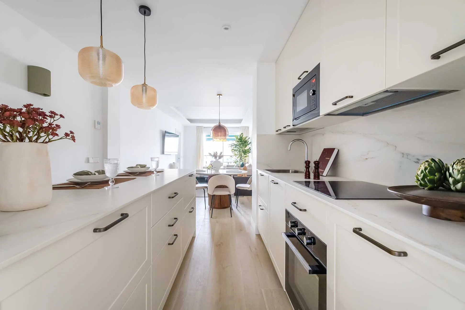Perspectiva de la cocina blanca alargada e integrada de estilo minimalista con detalles en mármol y barra americana