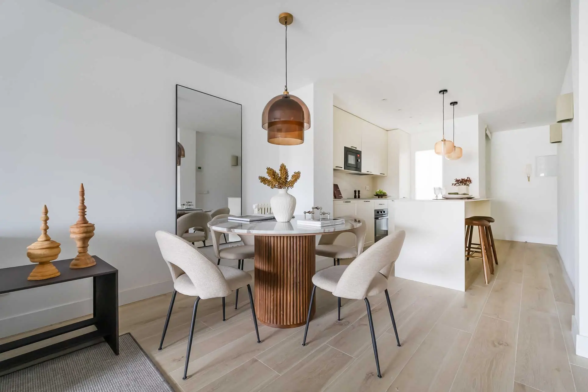 Zona del comedor con una mesa redonda de madera, sillas tapizadas y una elegante lámpara de suspensión ahumada