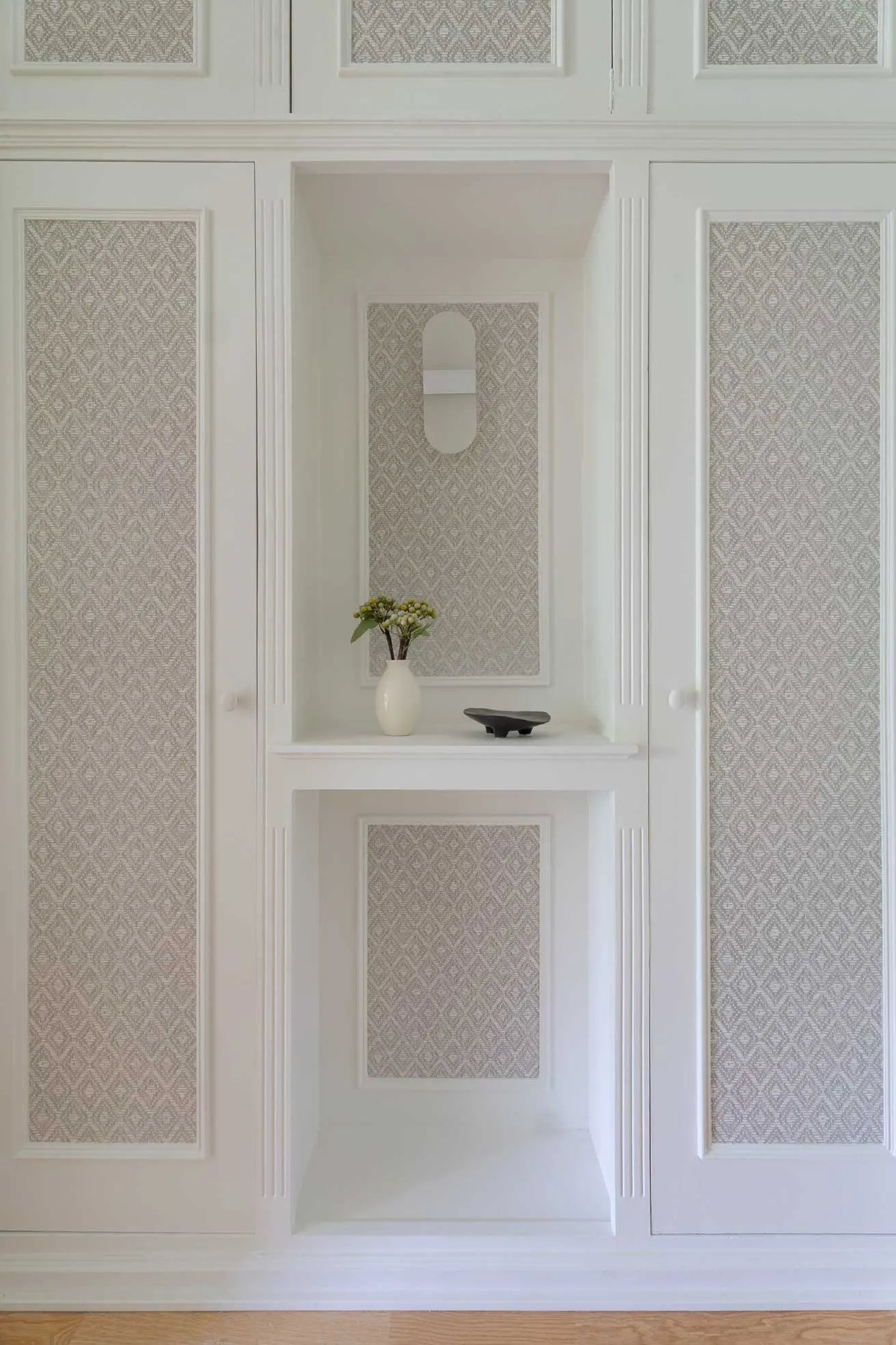 Detalle del mueble de armarios empotrados blancos con paneles texturizados y hornacina decorativa central