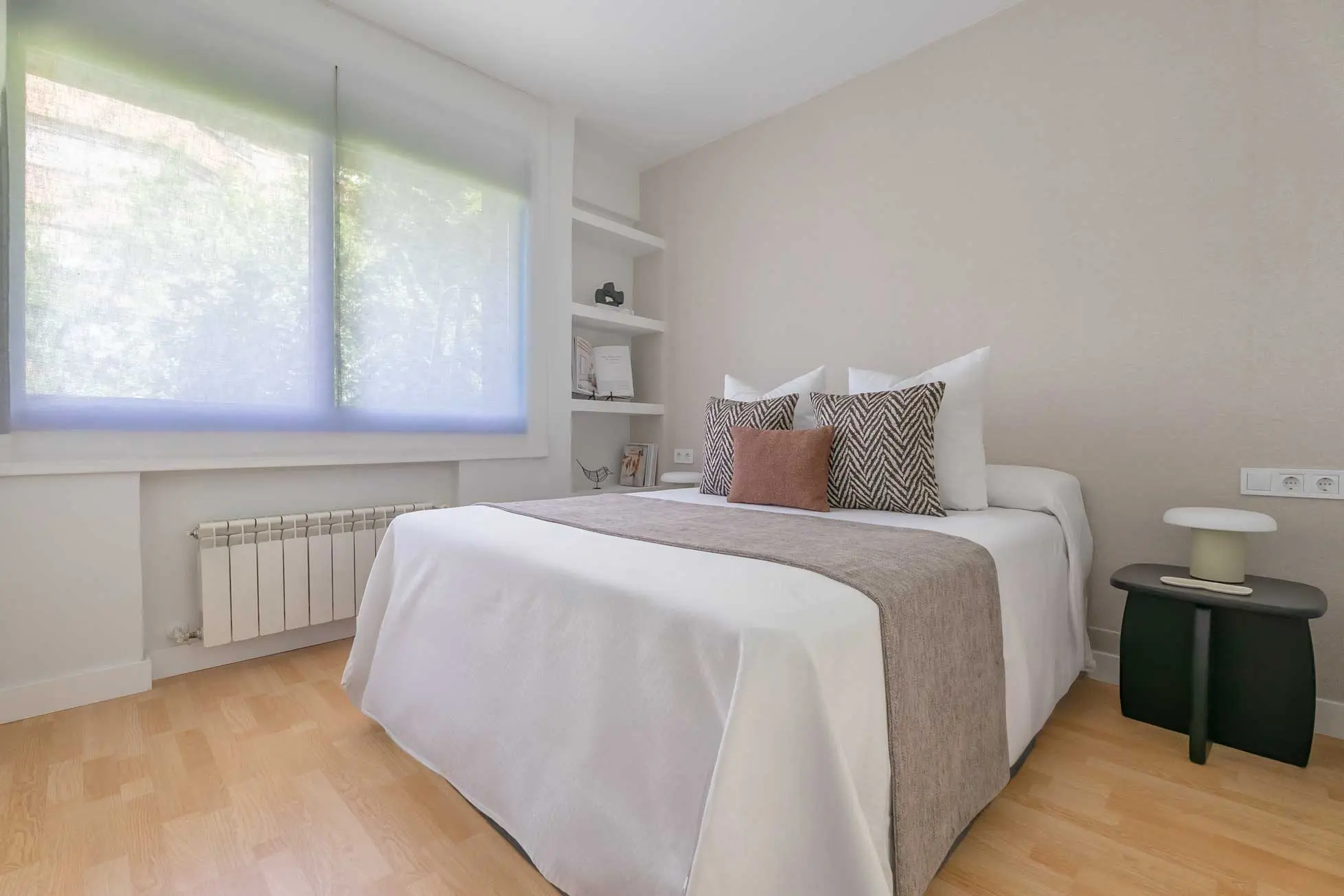 Dormitorio principal con cama doble perfectamente vestida, cojines estampados en zigzag y rincón de lectura junto a la ventana