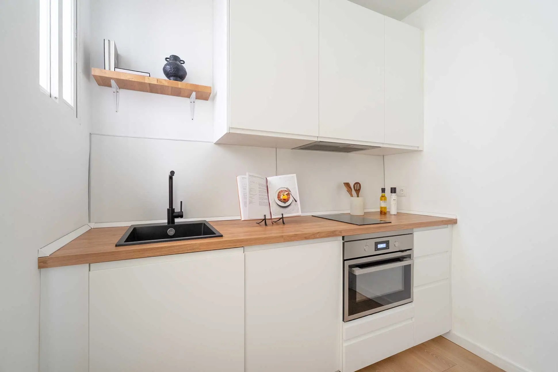Plano medio de la cocina de diseño minimalista blanca con encimera de madera, fregadero negro y libros de recetas en el soporte