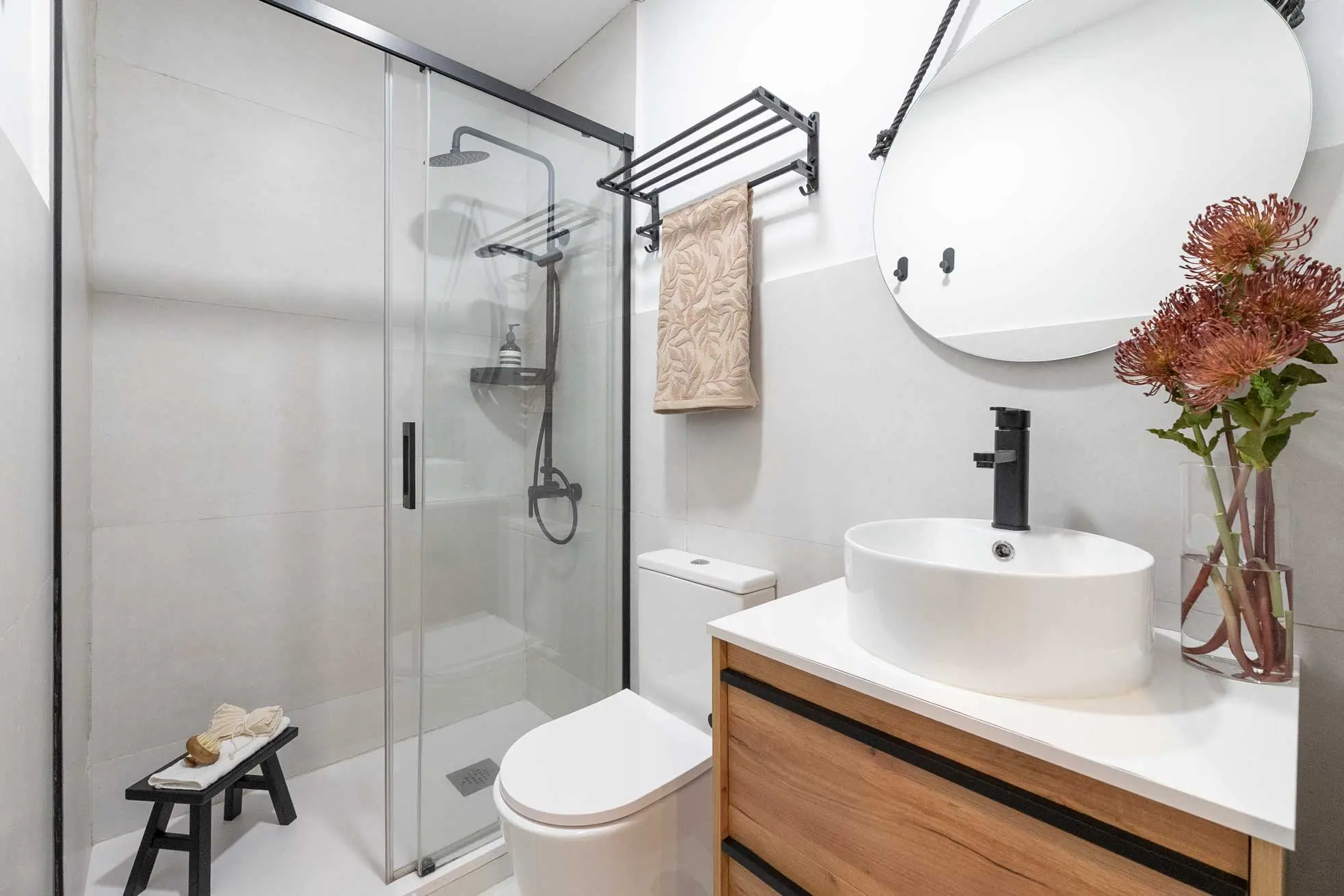 Cuarto de baño moderno con mueble suspendido de madera, lavabo de bol cerámico blanco, grifería negra y mampara de ducha a juego