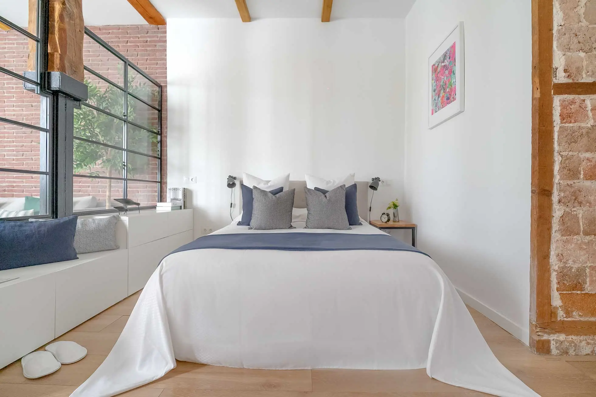 Plano frontal de la cama doble vestida con textiles blancos y camino azul marino, enmarcada por columnas de madera original