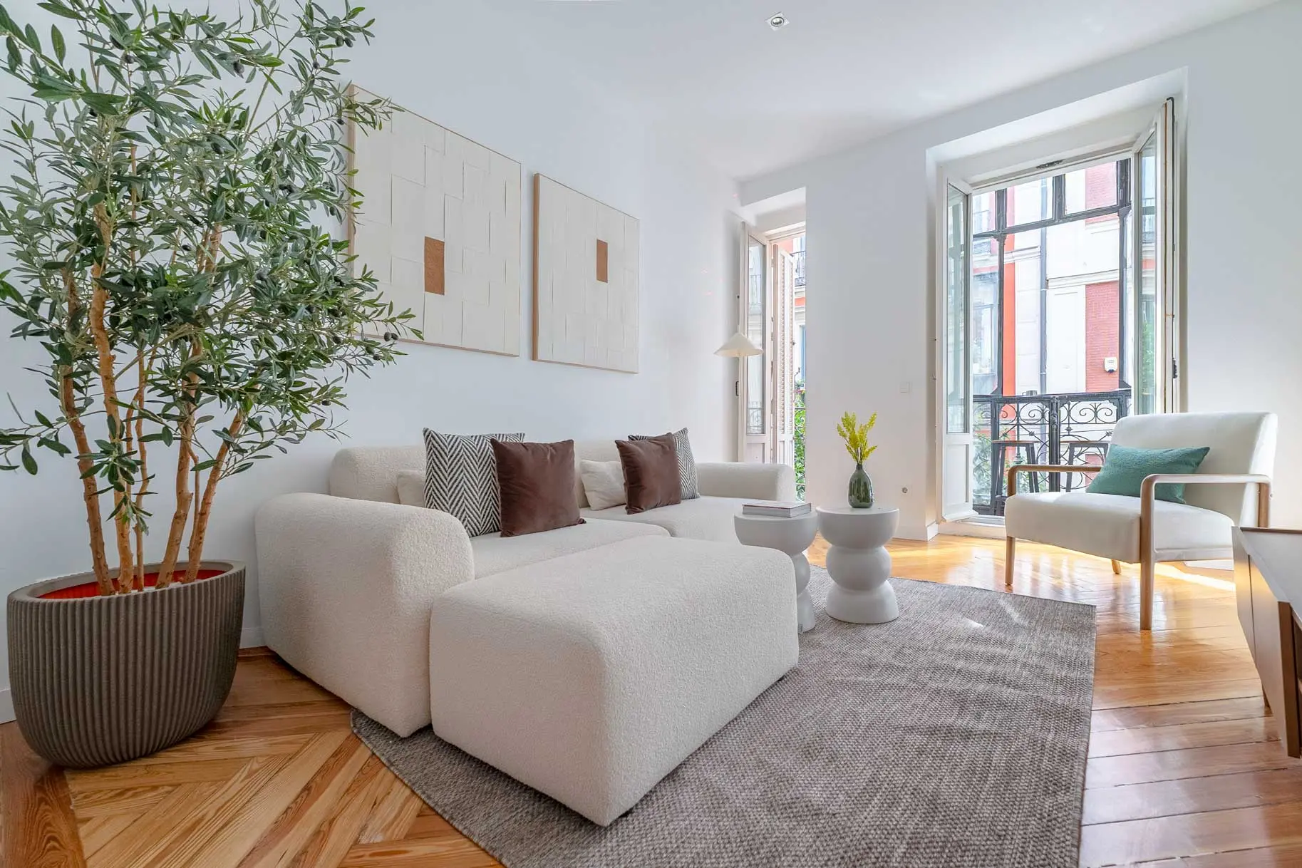 Vista general del salón de diseño con parqué en espiga, mobiliario orgánico en tonos claros y amplios balcones tradicionales
