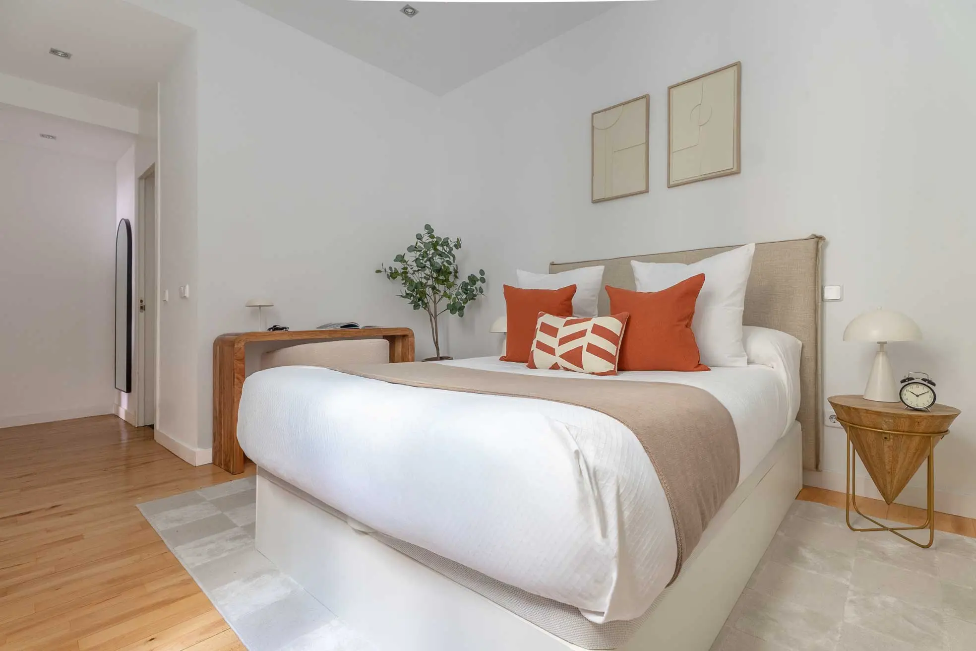 Dormitorio principal con cama doble perfectamente vestida, cojines decorativos color teja y escritorio de madera integrado