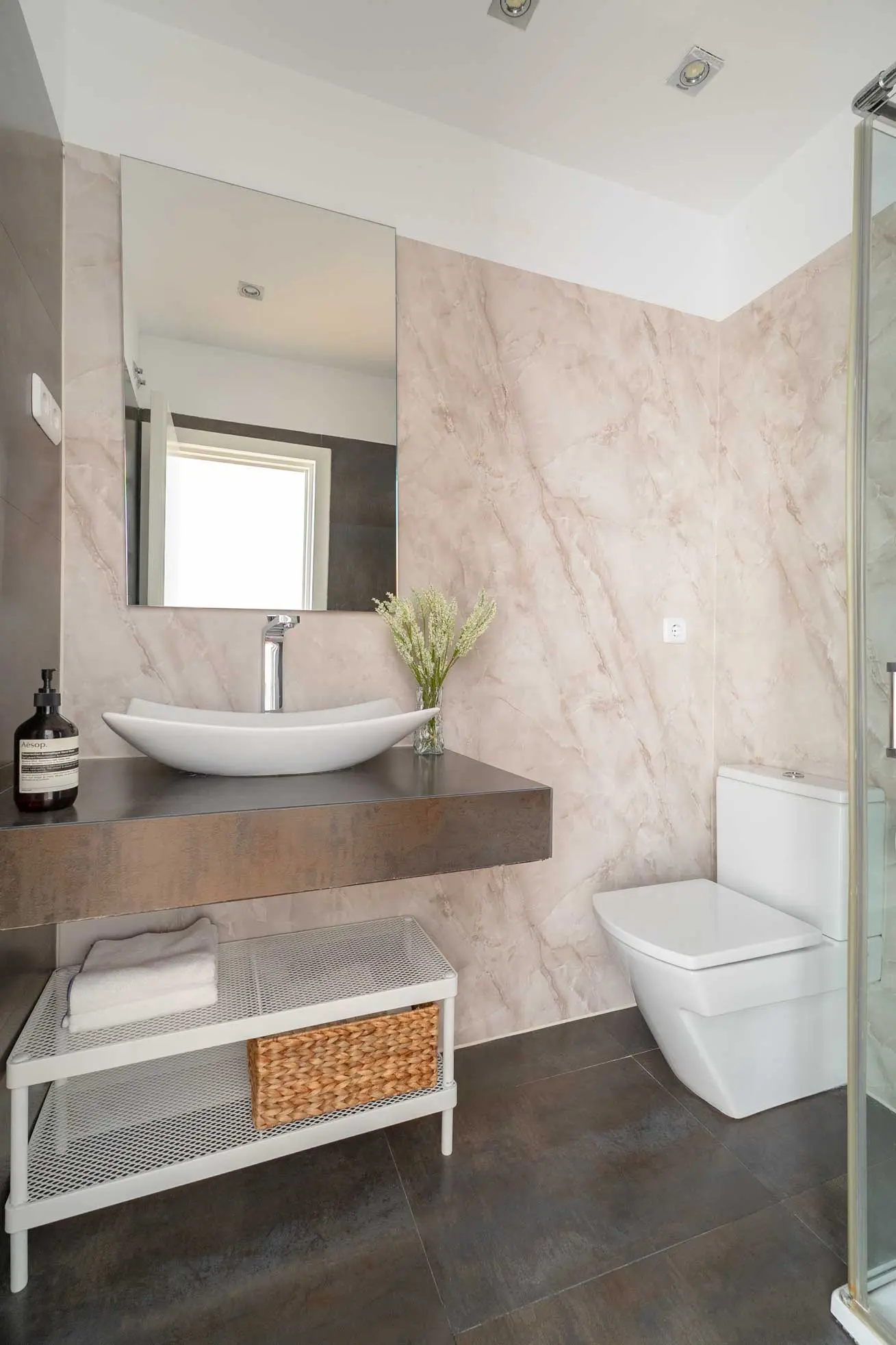 Cuarto de baño de cortesía con revestimiento cerámico efecto mármol rosa, lavabo de bol suspendido y espejo rectangular