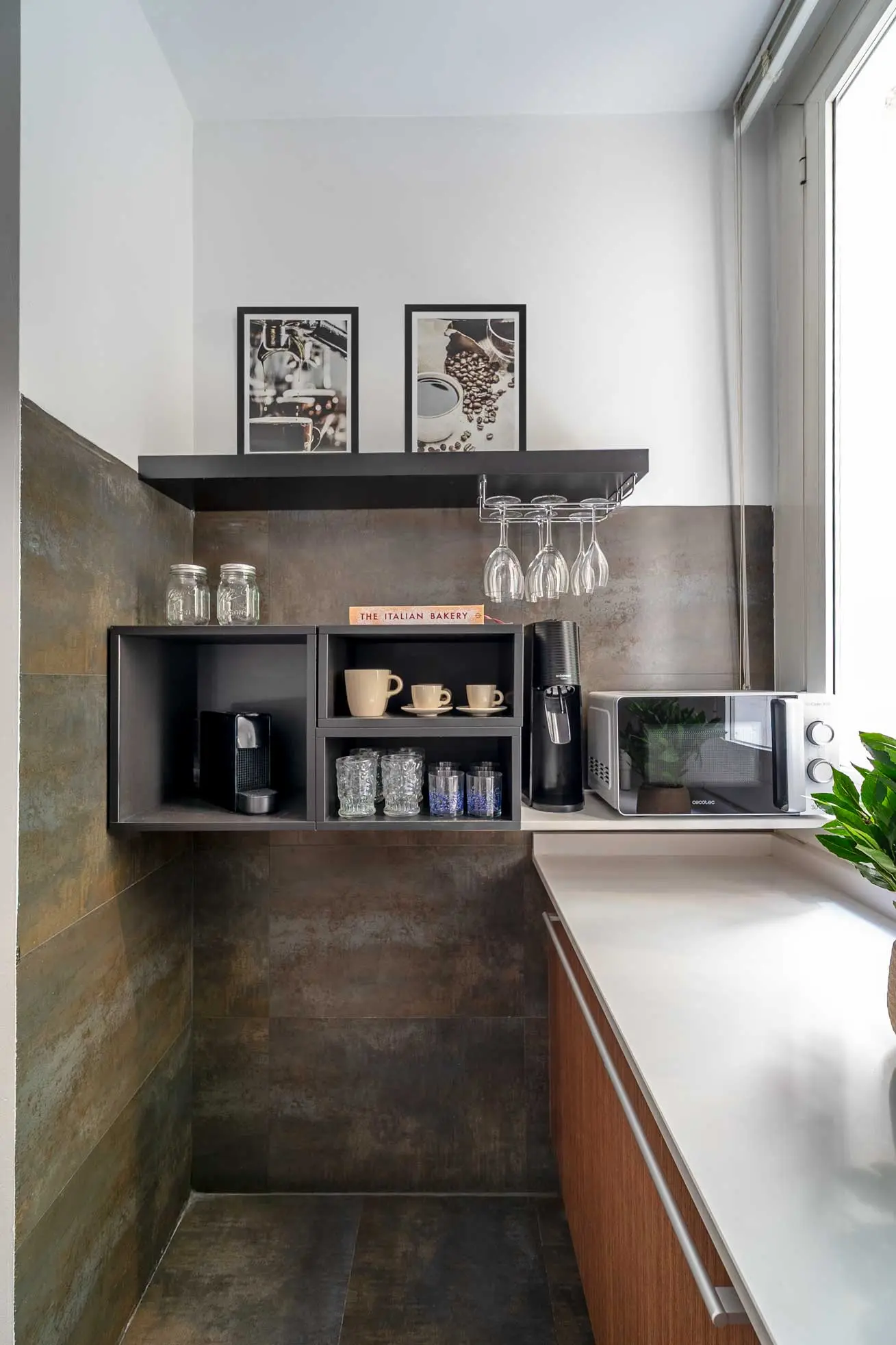 Detalle del rincón del café en la cocina con estanterías modulares negras, tazas cerámicas y cafetera integrada