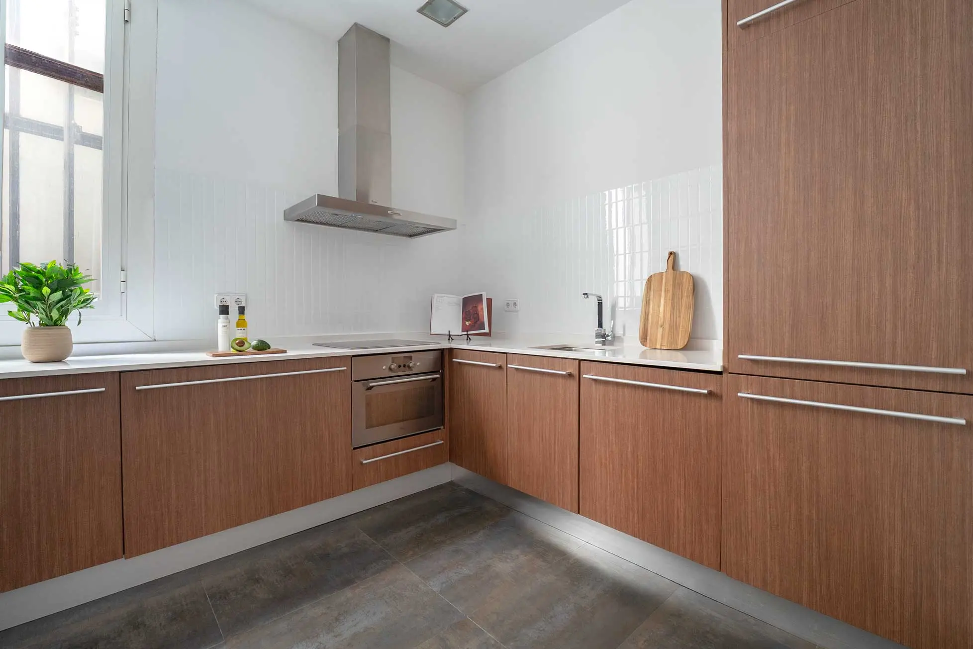 Perspectiva amplia de la cocina moderna con mobiliario texturizado en madera, encimera blanca y campana extractora de acero