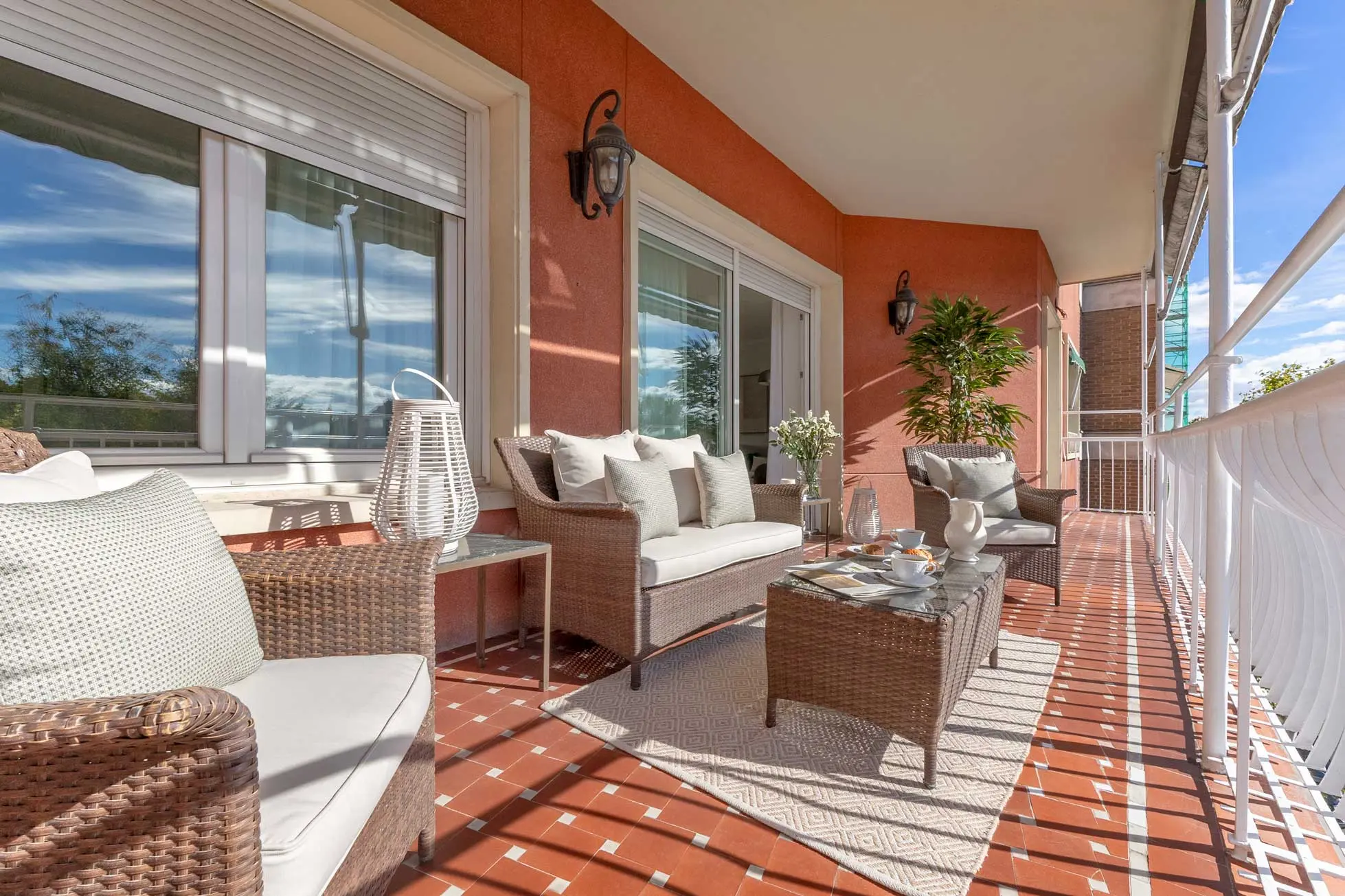 Ángulo longitudinal de la terraza mostrando la amplitud del espacio exterior, los sofás con cojines claros y farolillos decorativos