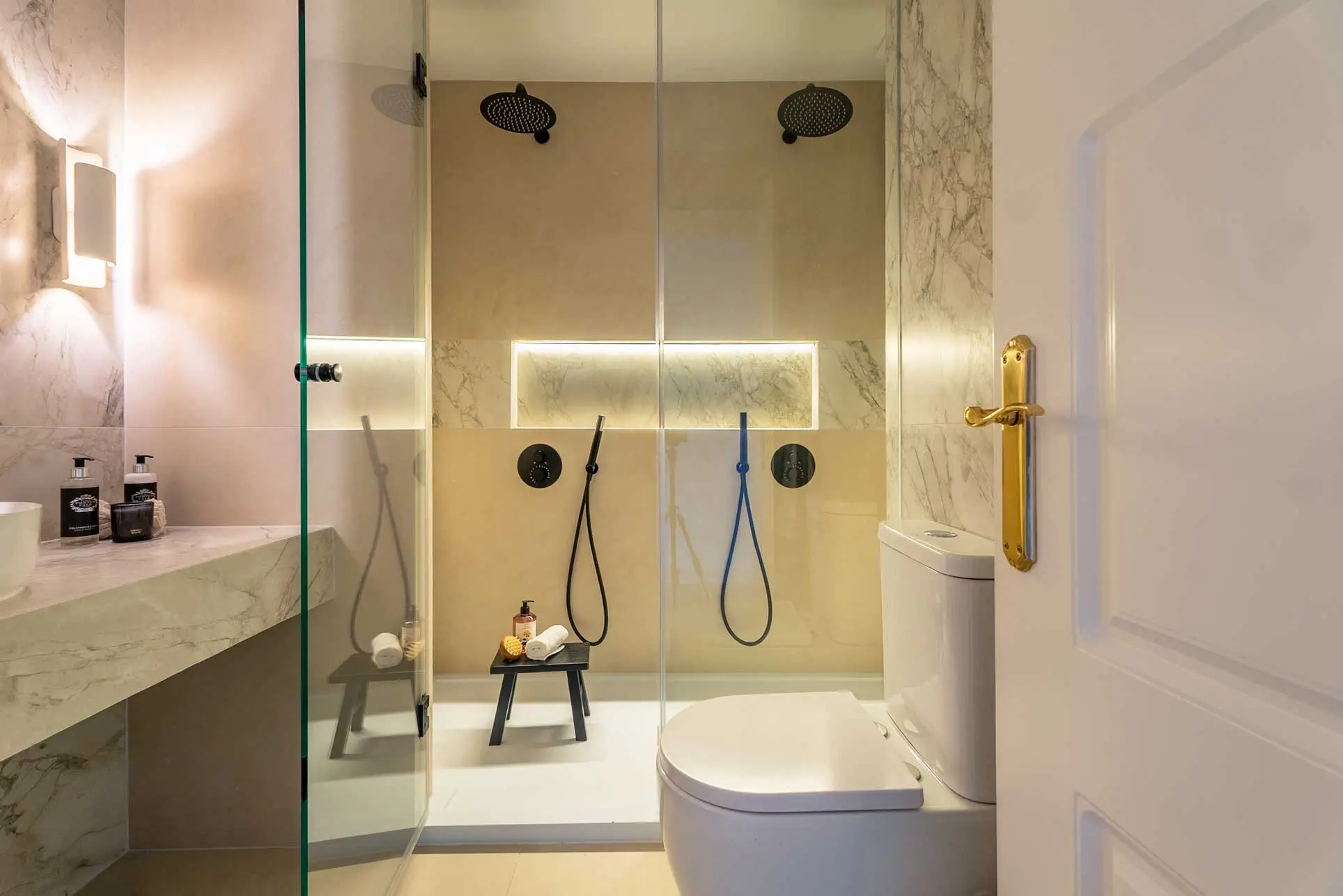 Zona de ducha doble premium con dos rociadores de techo negros, mampara de cristal transparente y azulejos efecto mármol blanco