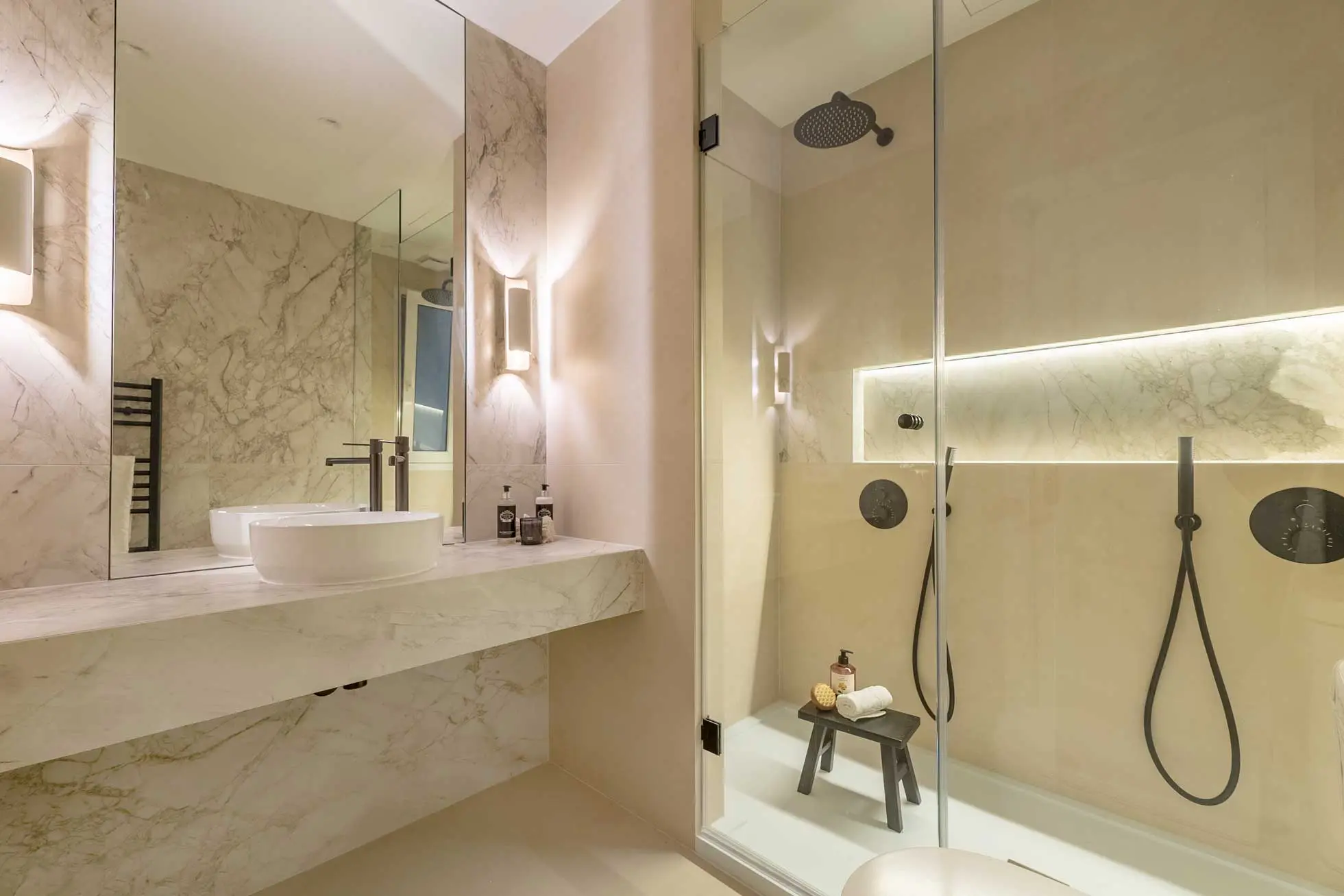 Perspectiva del mueble de baño flotante en mármol con lavabo de bol integrado, espejo retroiluminado y grifería negra de diseño