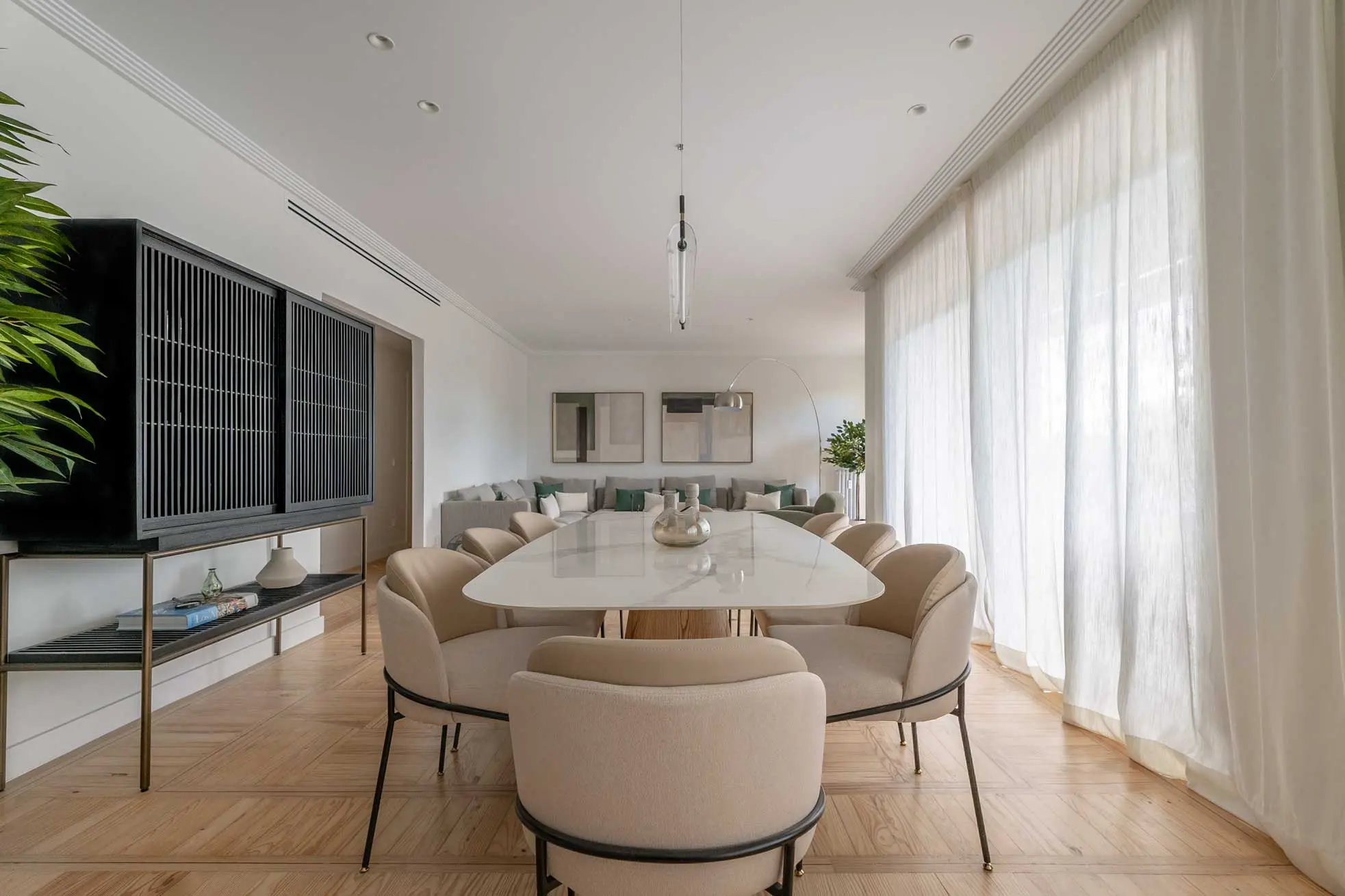 Plano frontal de la zona de comedor de alta gama presidida por una mesa de mármol blanco, sillas tapizadas y un gran aparador de madera negra eslatada