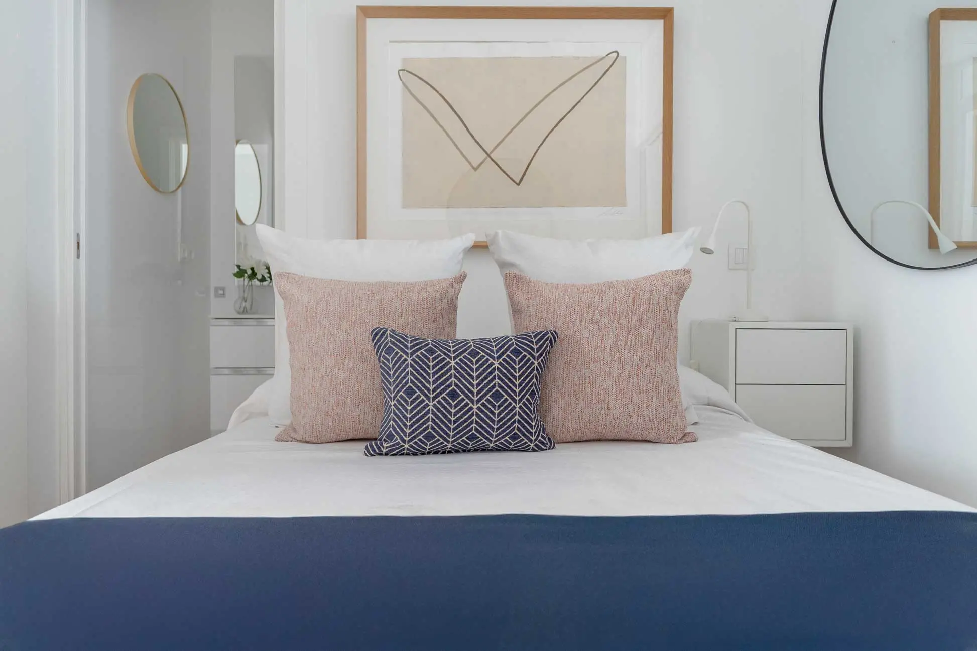 Plano frontal y simétrico de la cama de matrimonio destacando la combinación de cojines terracota y azul con un cuadro abstracto superior