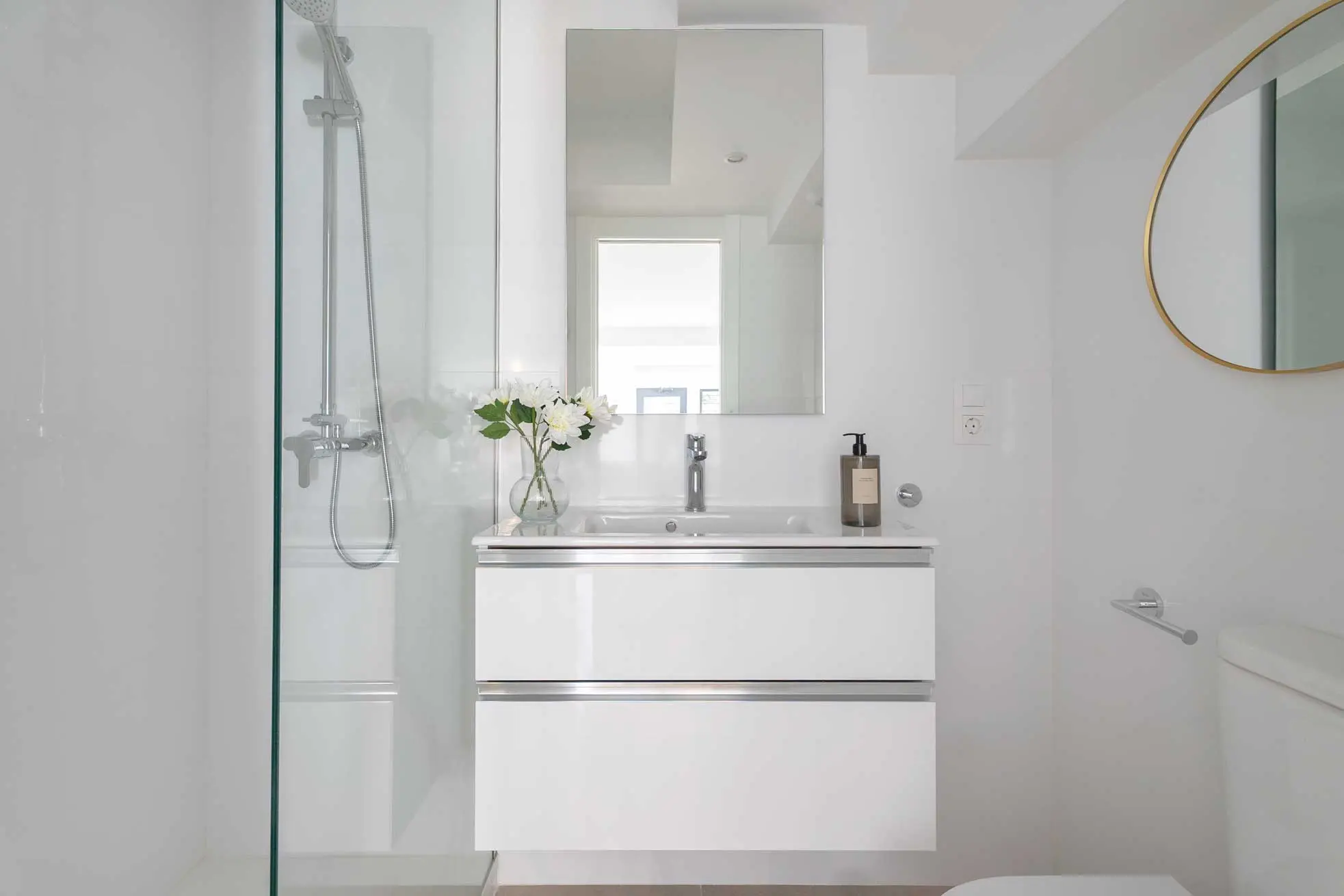 Cuarto de baño de líneas limpias con mueble de lavabo flotante blanco brillante, mampara de ducha de cristal y espejo con marco dorado