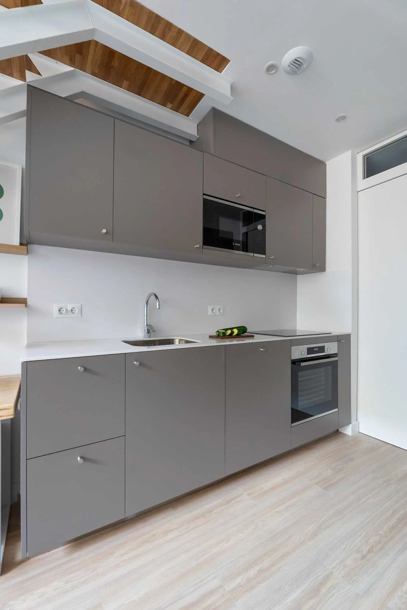 Cocina lineal minimalista con frentes de armarios en gris mate texturizado, encimera blanca y electrodomésticos integrados