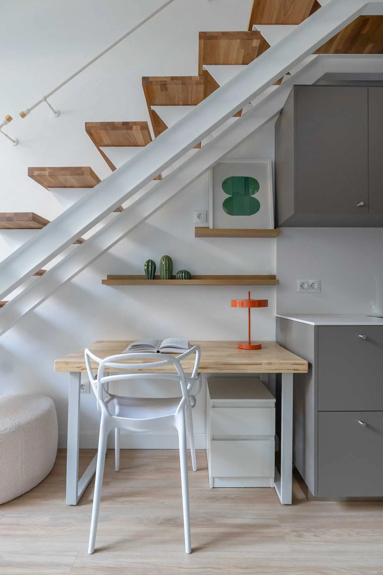 Rincón de escritorio o zona de estudio optimizada bajo el hueco de la escalera calada con una lámpara de mesa naranja de acento