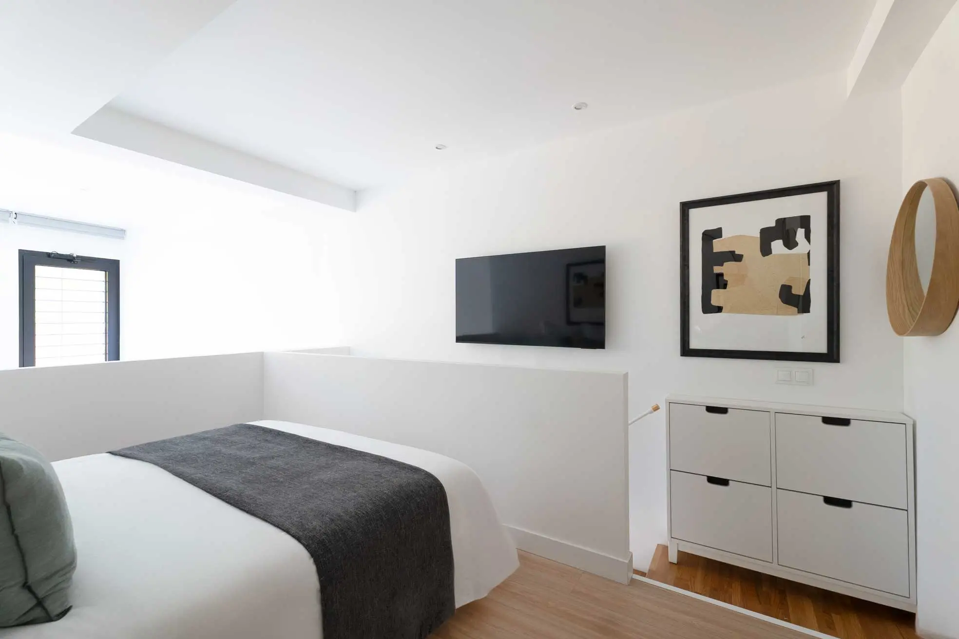 Encuadre lateral desde la planta alta mostrando la barandilla blanca del loft, el televisor empotrado y un mueble zapatero modular