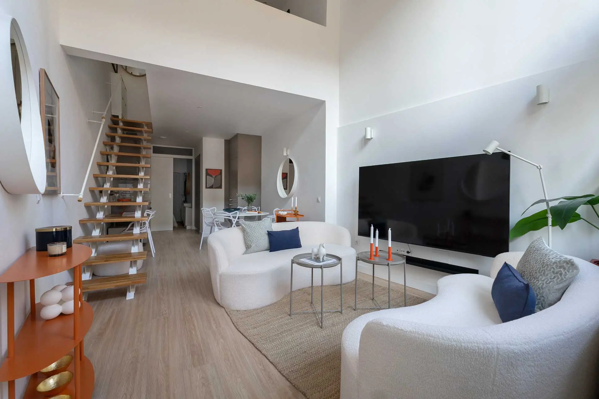 Perspectiva abierta en gran angular desde el salón de doble altura que muestra la escalera calada y la transición hacia la cocina y el comedor