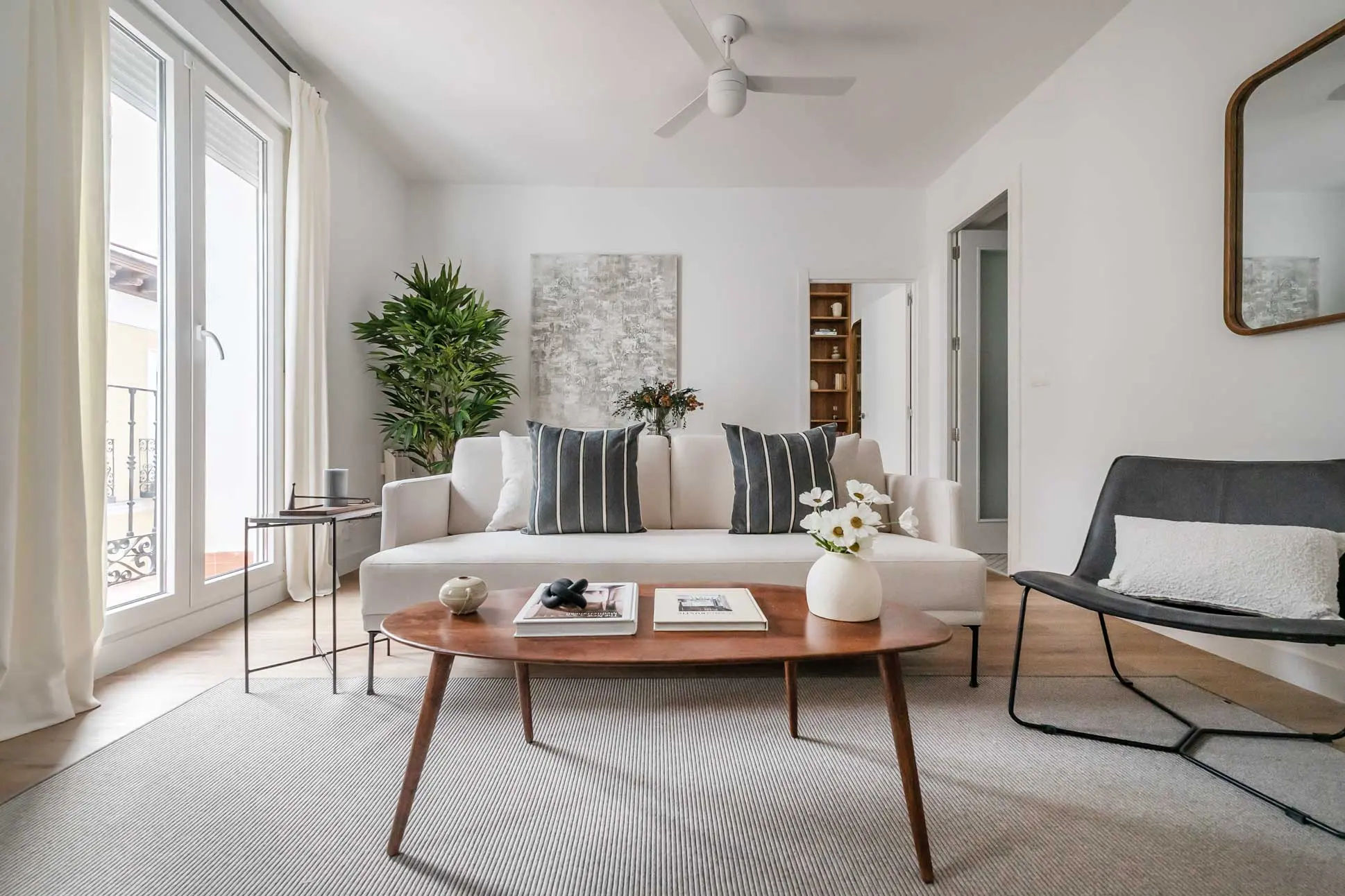 Plano medio del sofá beige en el salón enmarcado por un gran ventanal de acceso al balcón y una planta de interior