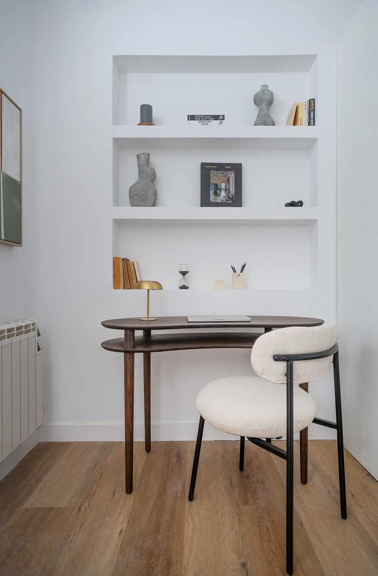 Rincón de trabajo o estudio con un escritorio elíptico de madera oscura, silla bouclé blanca y hornacinas decorativas empotradas