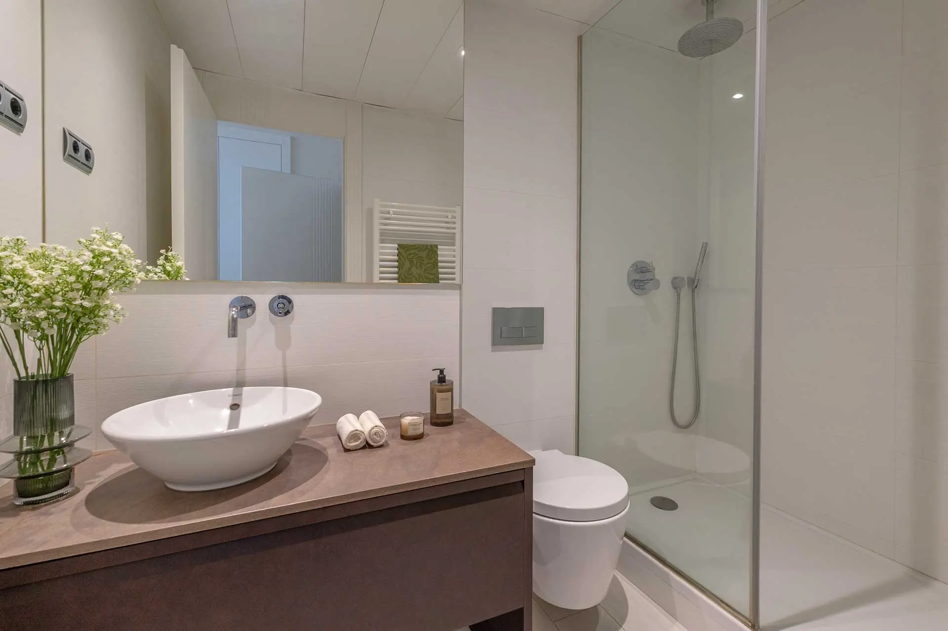 Cuarto de baño moderno con lavabo de bol cerámico sobre encimera oscura, grifería empotrada y plato de ducha con mampara de cristal