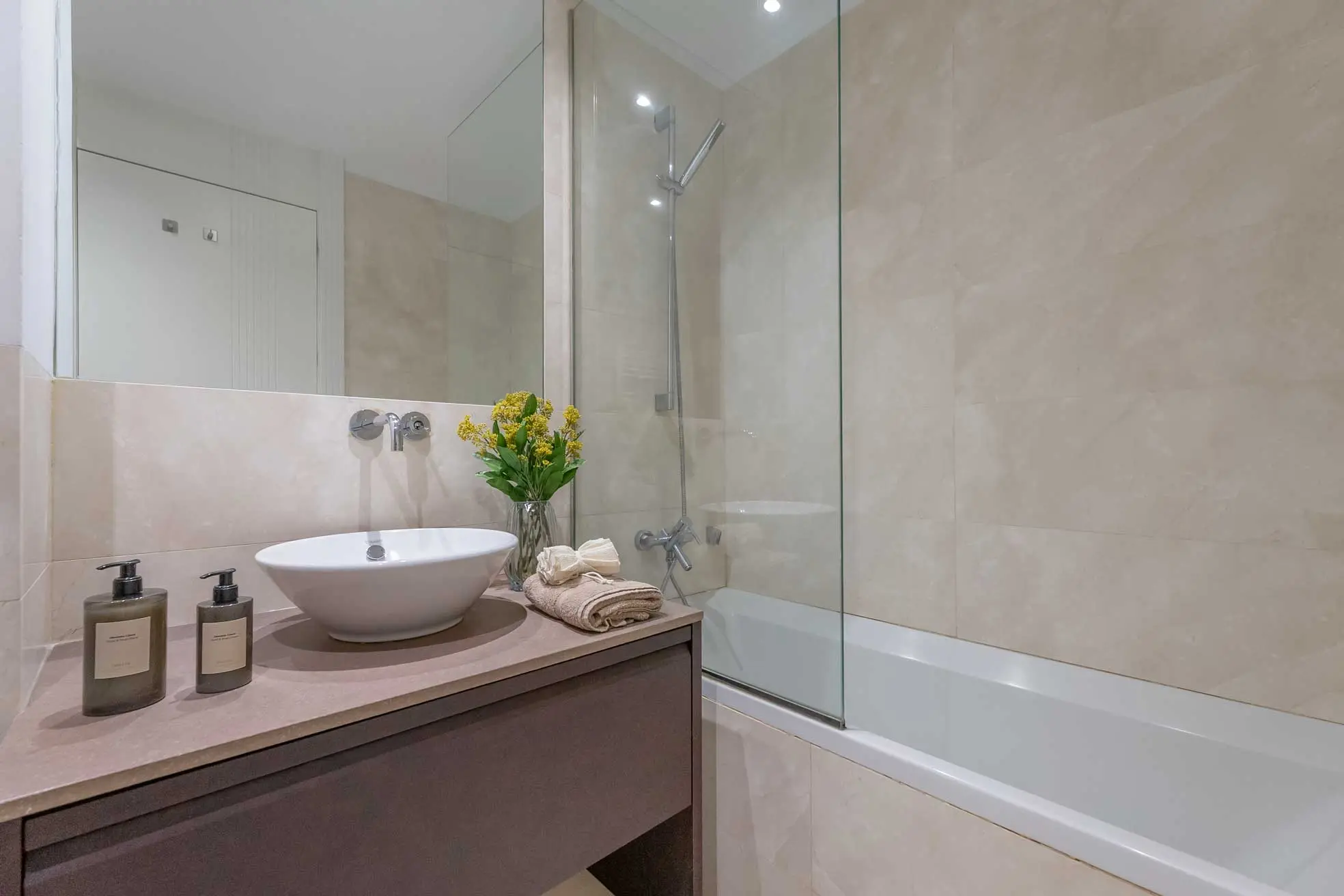 Segundo cuarto de baño integrado con bañera, revestimiento cerámico beige texturizado y lavabo suspendido moderno