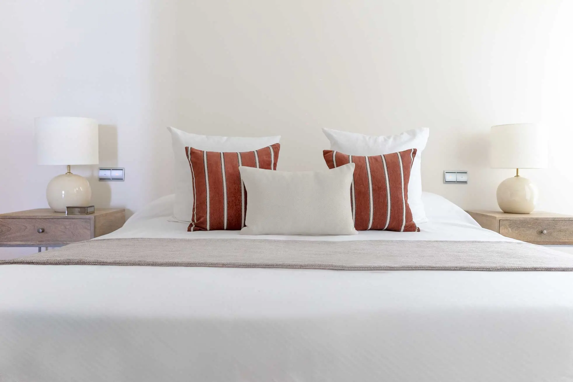 Plano de detalle simétrico del cabecero del dormitorio principal con almohadones premium y lámparas de noche esféricas
