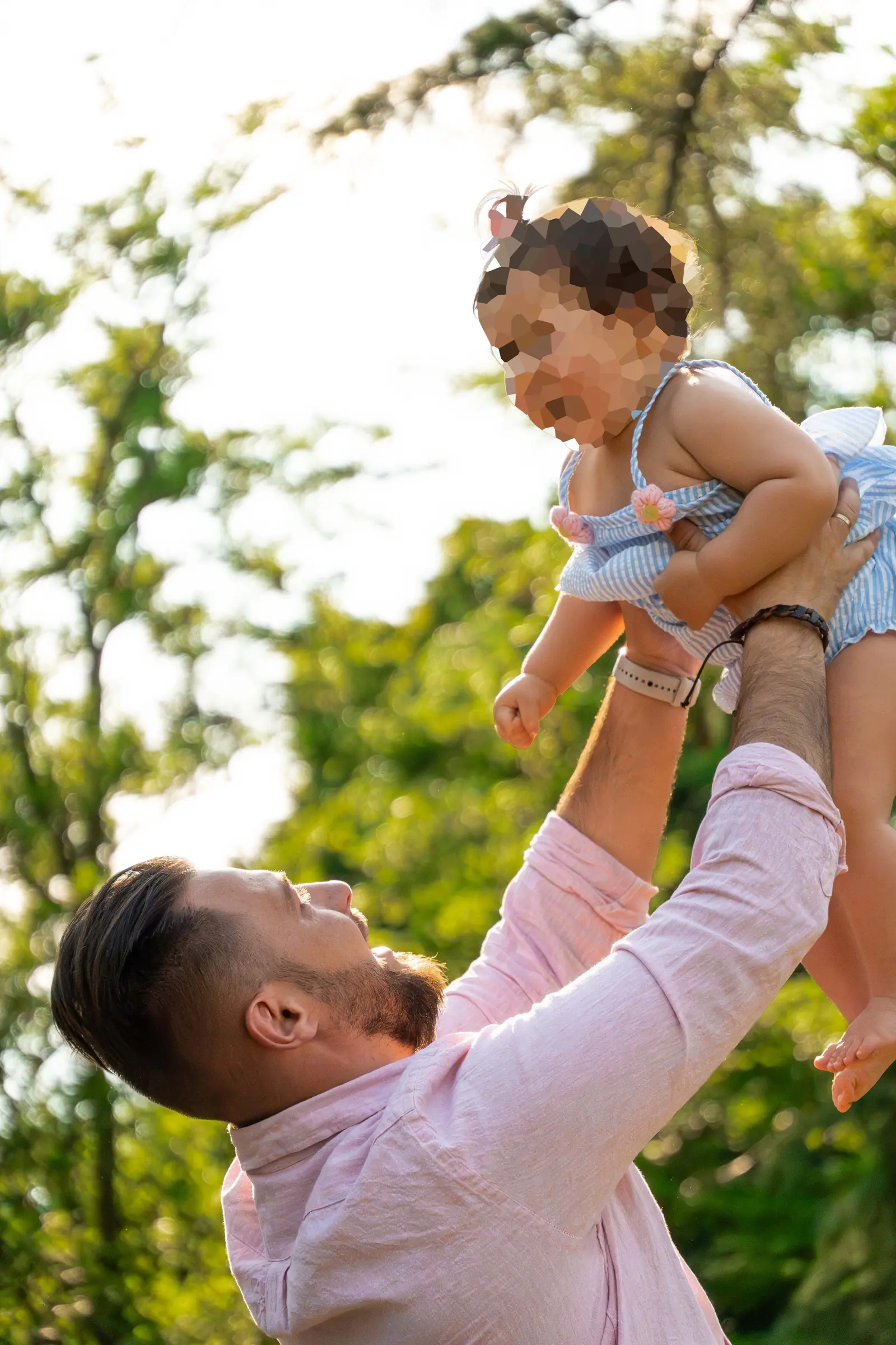 Los dos padres riendo a carcajadas mientras sostienen en brazos a su hija en el parque.