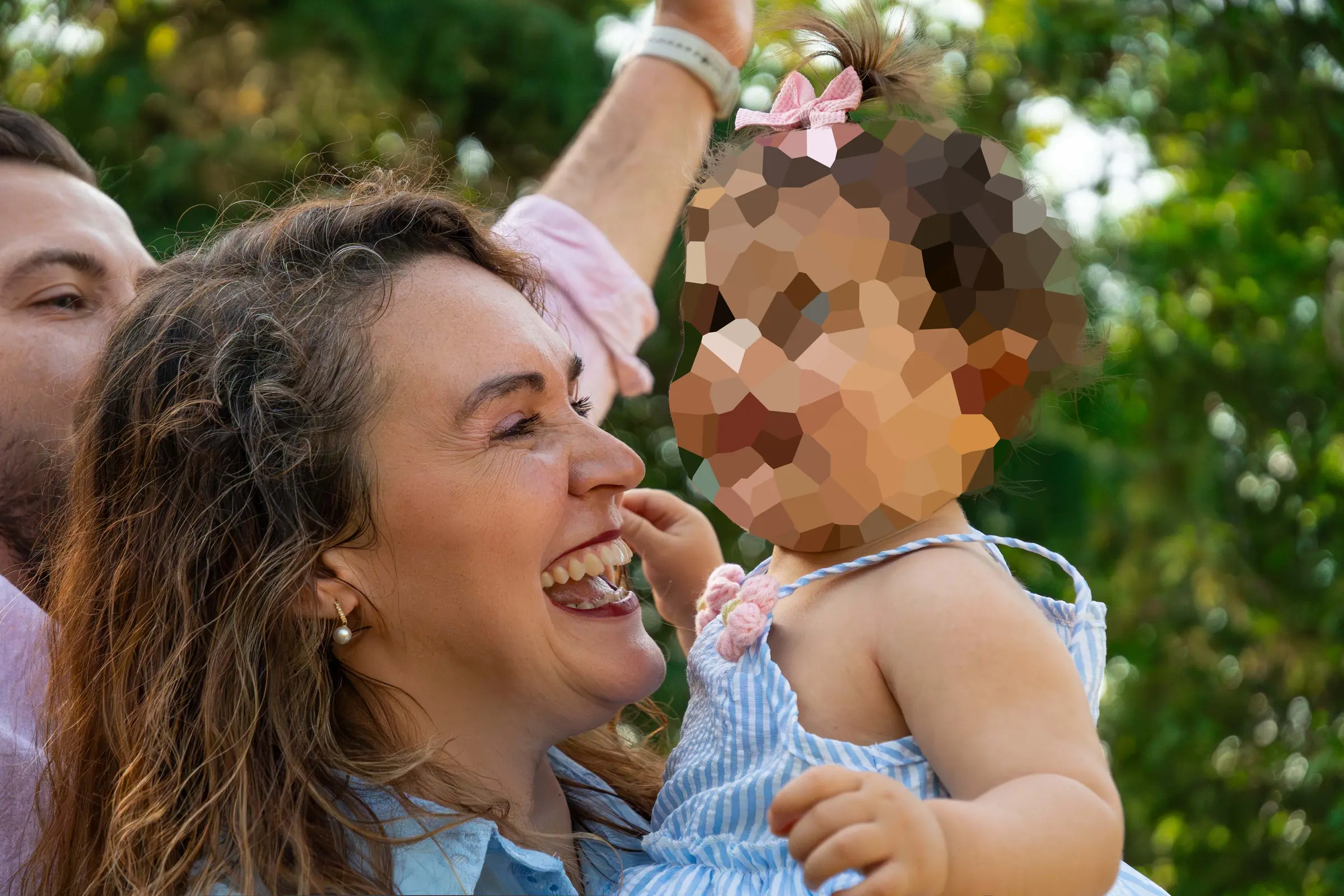 Retrato de la familia al completo agachada en el césped: los padres sostienen las manos de su hija mientras da sus primeros pasos.