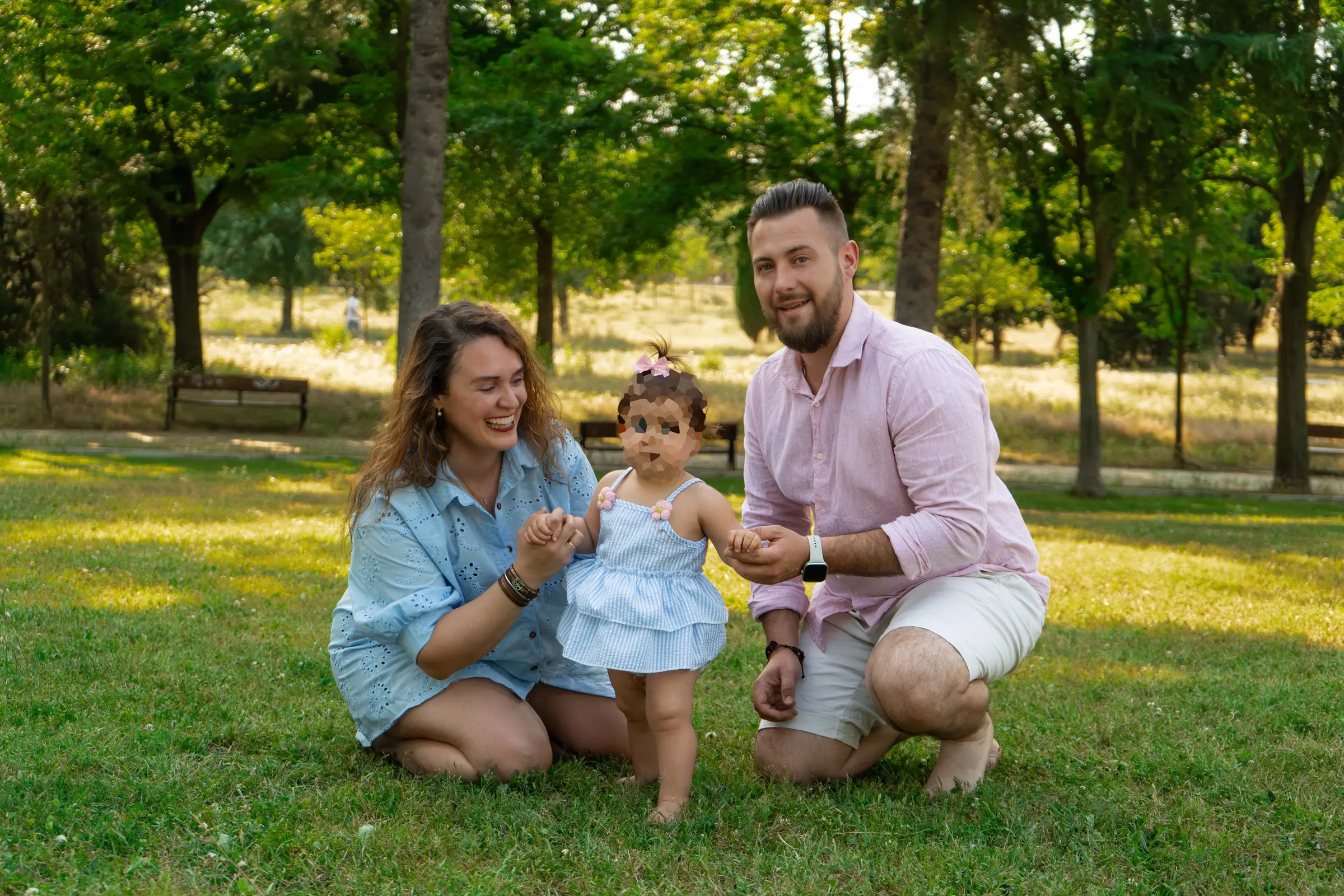 Contrapicado de unos padres levantando alegremente en vilo a su pequeña hija contra un cielo azul luminoso y soleado en un parque de Madrid.