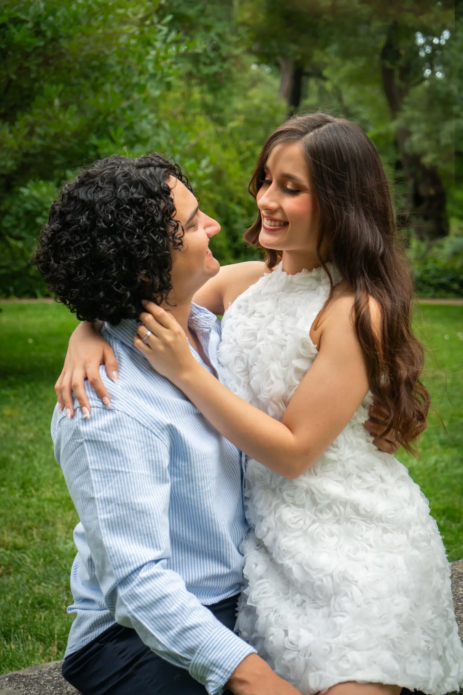 La pareja sentada y abrazada; ella le rodea el cuello con los brazos y se miran sonriendo, sobre un fondo verde.